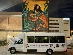 Night view of trolley bus parked below Rialto Theatre mural of woman with guitar.