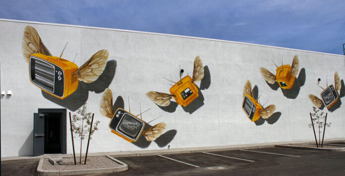 Yellow vintage televisions with wings painted across a large wall near Tucson’s Five Points area.