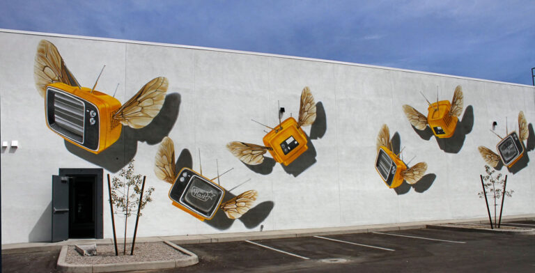 Yellow vintage televisions with wings painted across a large wall near Tucson’s Five Points area.
